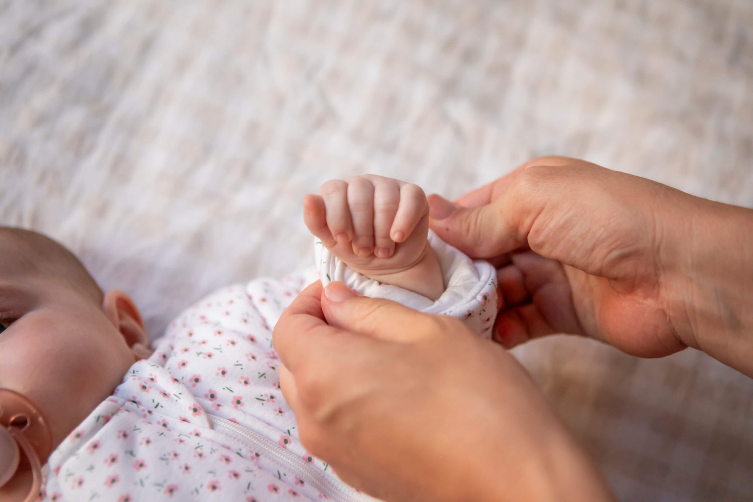Close-up of a baby's hand being adjusted in sleepsuit by an adult's hand on a neutral surface