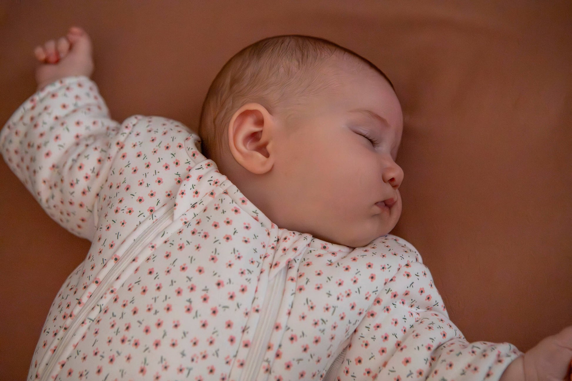 Baby sleeping peacefully in a floral sleepsuit against a neutral background