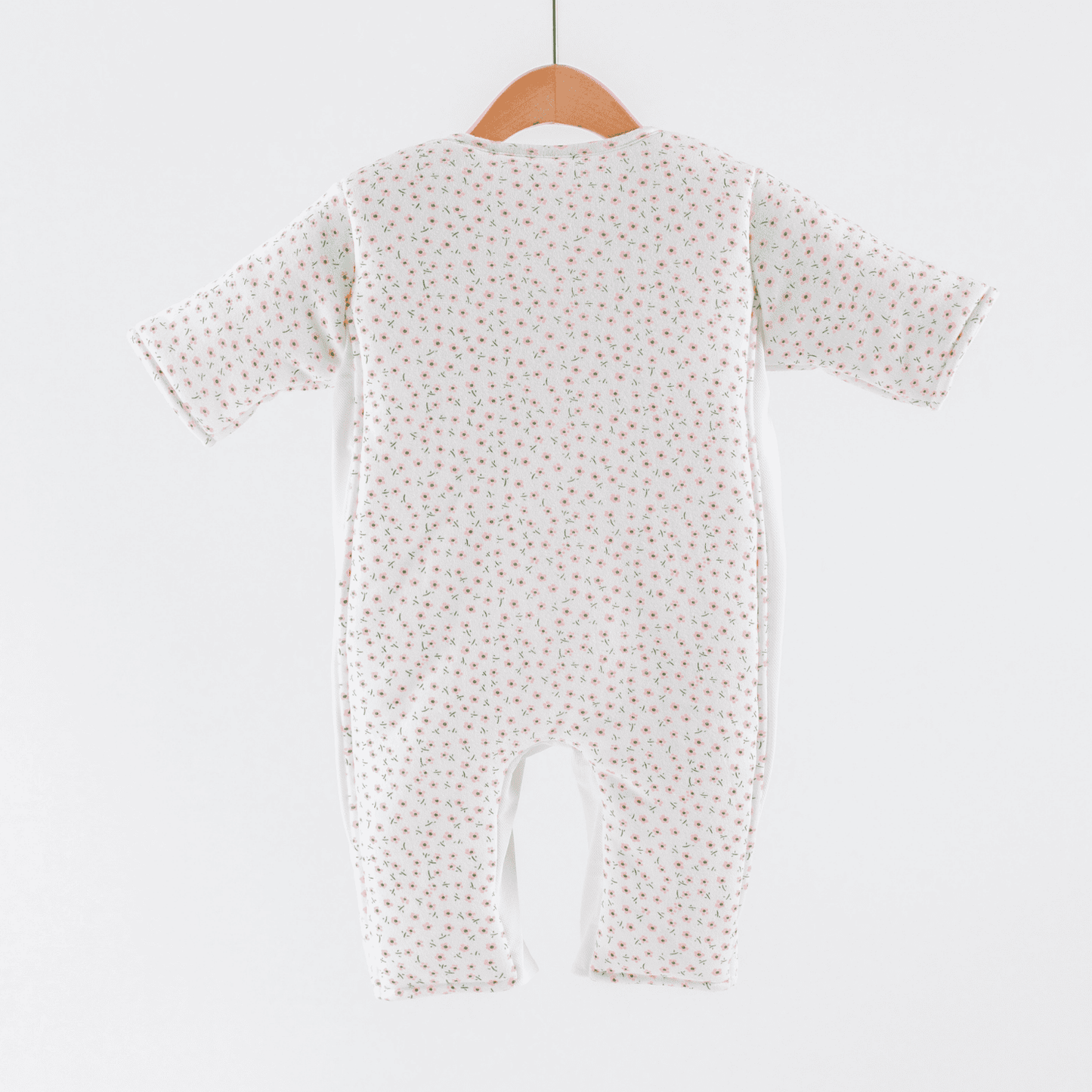Baby sleepsuit with  pink flower print pattern on a hanger against a white background