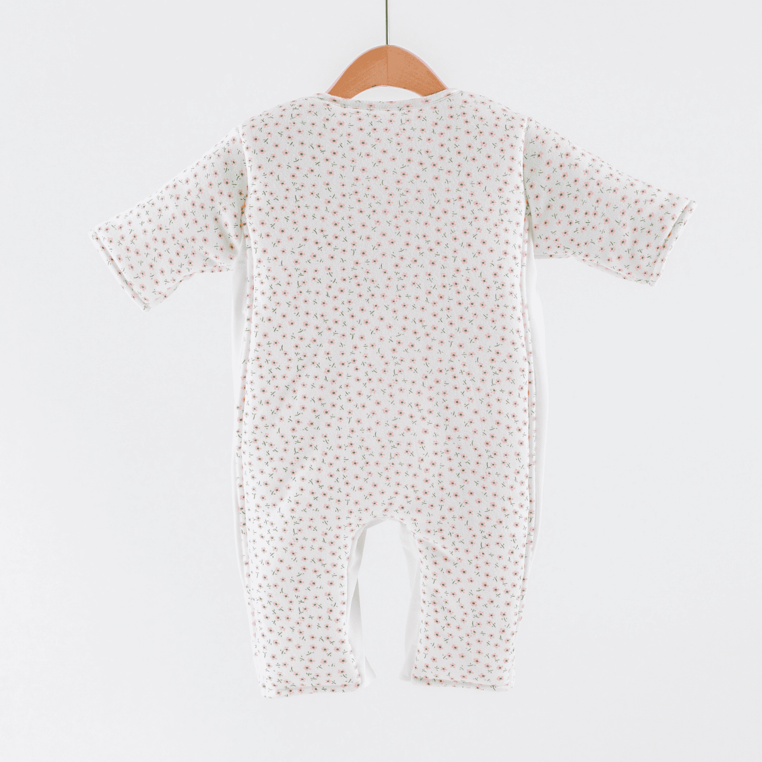 Baby sleepsuit with  pink flower print pattern on a hanger against a white background