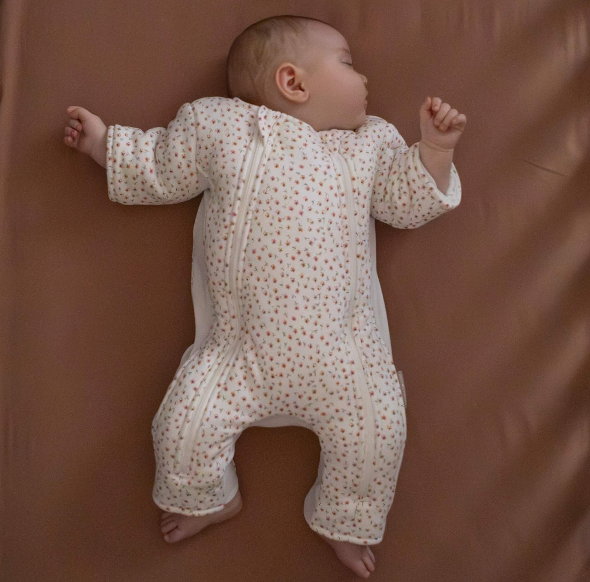 Baby sleeping in a floral sleepsuit lying on a brown surface