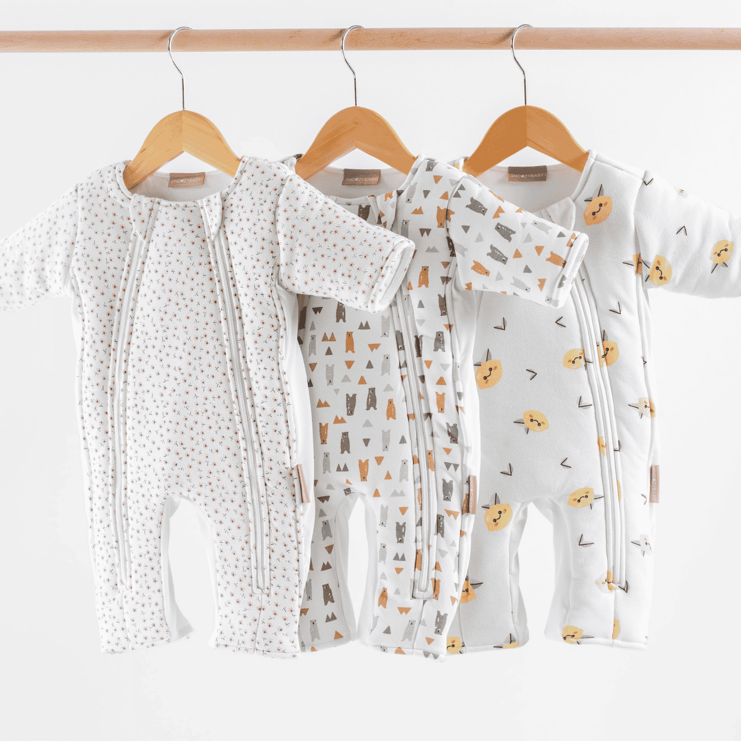 Baby transition swaddles with different patterns hanging on wooden hangers against a white background