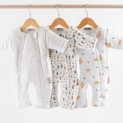 Baby transition swaddles with different patterns hanging on wooden hangers against a white background