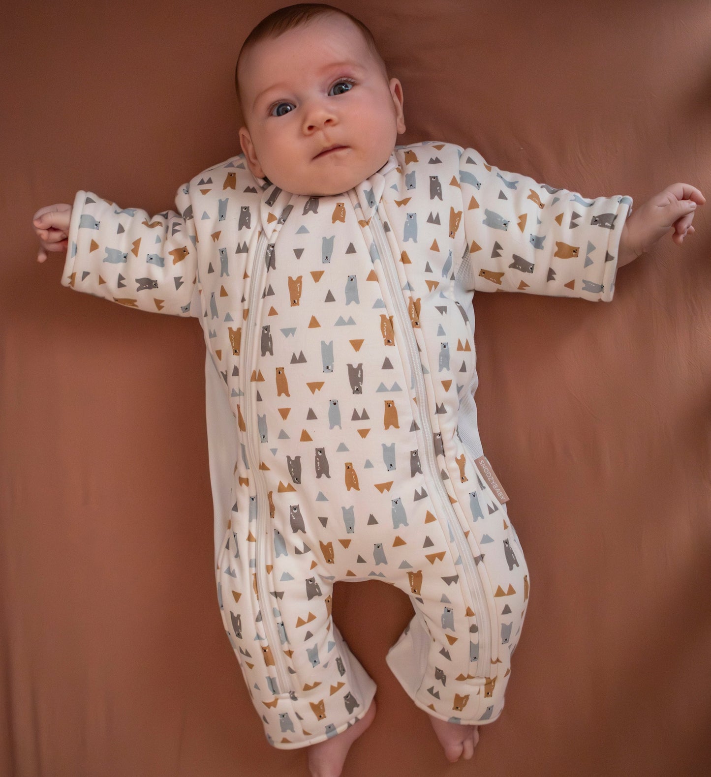 Baby wearing forest friends transition suit in cot on neutral sheet